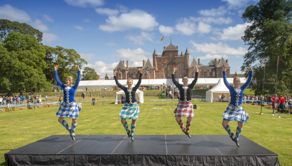 Highland dancers dancing in kilts on a stage in a field